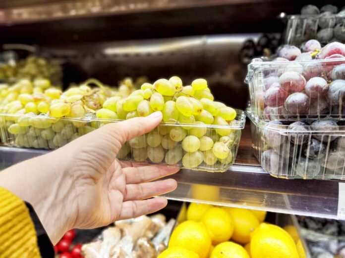 A,Person,Is,Reaching,For,A,Container,Of,Green,Grapes