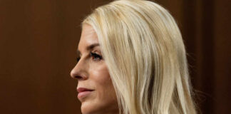 Profile view of a woman with blonde hair in business attire, displaying a serious expression