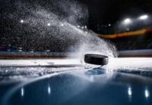 Olympic Hero Stuns: First Hockey Medal in 46 Years A black hockey puck sliding across an ice rink with ice particles flying around it