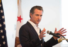 A man in a suit speaking into a microphone with a California flag in the background