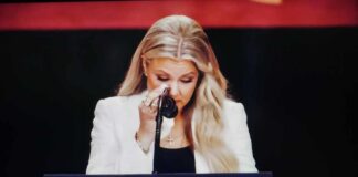 A woman in formal attire wiping her tears while speaking at a podium