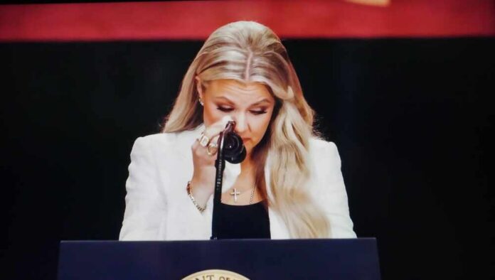A woman in formal attire wiping her tears while speaking at a podium