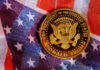A commemorative coin featuring the presidential seal and the name Donald Trump on an American flag background