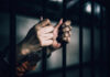 ICE’s Shocking Street Arrest Dangers Exposed Hands gripping prison bars in a dimly lit environment