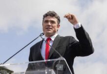 A man in a suit speaking passionately at a podium during an outdoor event