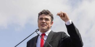 A man in a suit speaking passionately at a podium during an outdoor event
