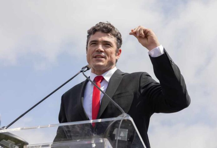 A man in a suit speaking passionately at a podium during an outdoor event