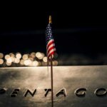 A small American flag positioned in front of the word 'PENTAGON' on a reflective surface