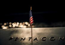 A small American flag positioned in front of the word 'PENTAGON' on a reflective surface