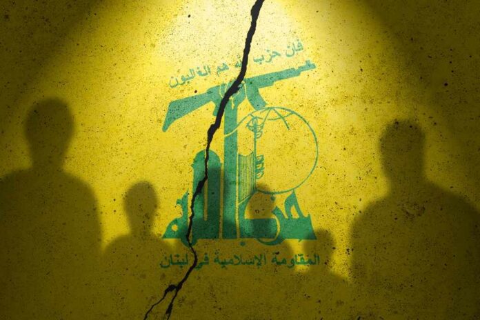 shutterstock_2373422413.jpg Silhouettes of two figures against a yellow background featuring Hezbollah's emblem
