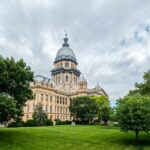 Historic government building surrounded by trees and grass under a cloudy sky