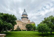 Historic government building surrounded by trees and grass under a cloudy sky
