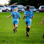 Two girls running on a soccer field during a game