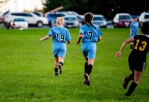Two girls running on a soccer field during a game