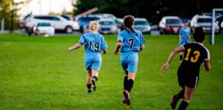 Two girls running on a soccer field during a game