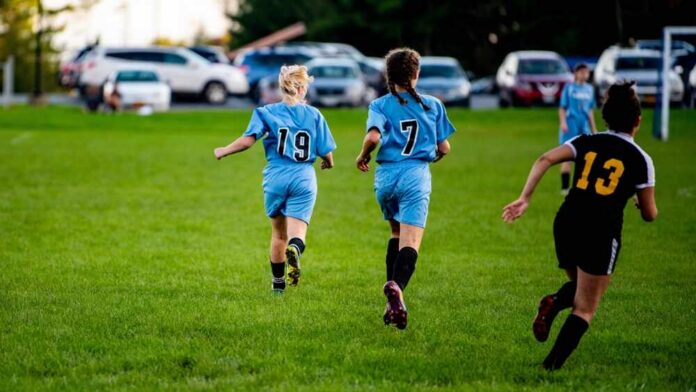Two girls running on a soccer field during a game