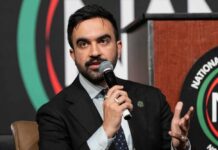 A speaker at a conference holding a microphone and gesturing while speaking