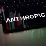 Mobile phone displaying the word 'ANTHROPIC' over a background of financial graphs