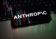 Mobile phone displaying the word 'ANTHROPIC' over a background of financial graphs