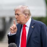 A political figure gesturing with a finger raised during a press conference