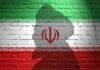Silhouette of a figure against the Iranian flag painted on a brick wall