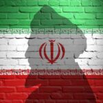 Silhouette of a figure against the Iranian flag painted on a brick wall