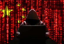 A hooded figure sitting in front of a laptop with a red digital background