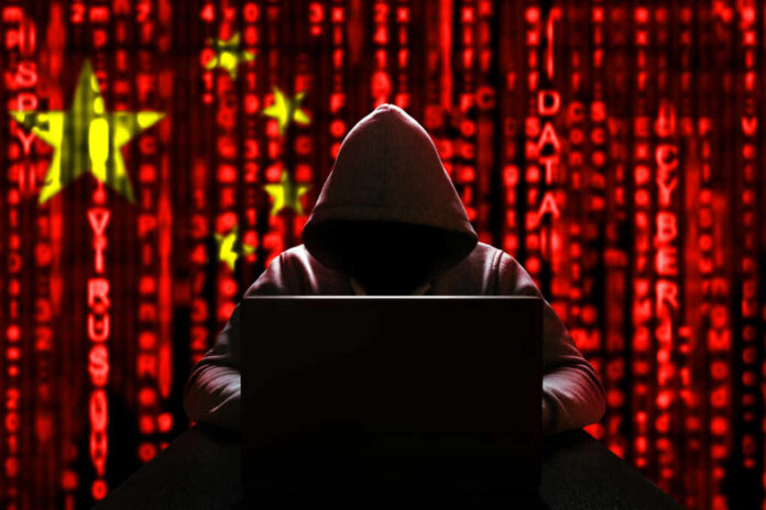 A hooded figure sitting in front of a laptop with a red digital background