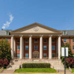Front view of a historic brick building with columns and landscaped grounds