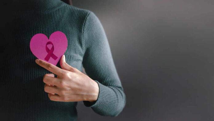shutterstock_1995360812.jpg Person holding a pink heart with a ribbon symbol