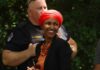 Smiling woman in a red headscarf at a community event with a police officer in the background