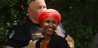 Smiling woman in a red headscarf at a community event with a police officer in the background