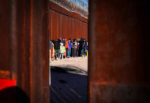 A line of people waiting near a border wall with barbed wire