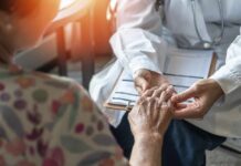 A doctor holding the hand of an elderly patient during a consultation