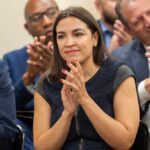 A woman in a dark dress clapping at a political event with an engaged audience in the background