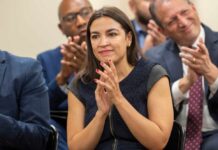 A woman in a dark dress clapping at a political event with an engaged audience in the background