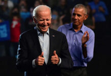 Joe Biden smiling and giving thumbs up while Barack Obama applauds in the background