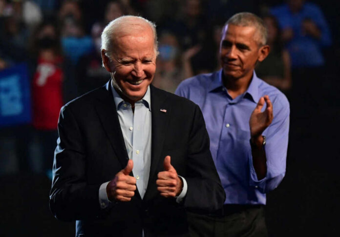 shutterstock_2502169807.jpg Joe Biden smiling and giving thumbs up while Barack Obama applauds in the background