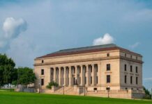 A historic building with columns and a red roof set against a cloudy sky