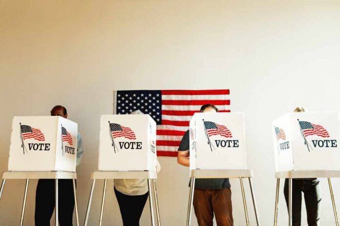 Individuals casting their votes in a polling station with an American flag in the background