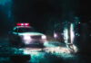 A police car with flashing lights at the scene of a flipped vehicle accident