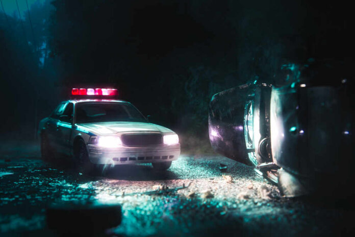 A police car with flashing lights at the scene of a flipped vehicle accident