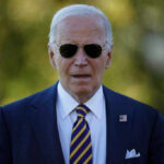Man wearing sunglasses and a suit with an American flag pin