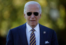 Man wearing sunglasses and a suit with an American flag pin