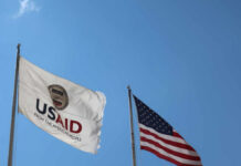 USAID flag and American flag waving against a clear blue sky