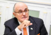 A man in a pinstripe suit with glasses, engaged in a thoughtful discussion