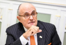 A man in a pinstripe suit with glasses, engaged in a thoughtful discussion