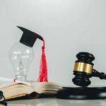 Light bulb with graduation cap beside open law book and judge’s gavel