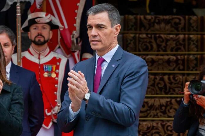 A government official speaking at a public event with an audience in the background