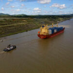 A cargo ship being assisted by a tugboat in a canal